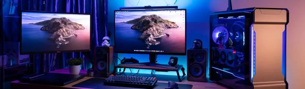 Setup de PC gamer completo com dois monitores, teclado mecânico, gabinete iluminado com LEDs e caixas de som na mesa.